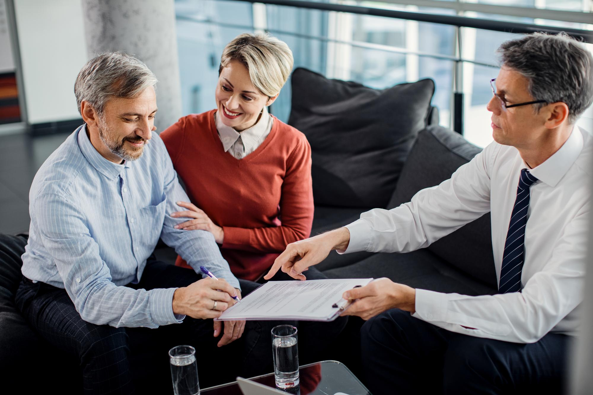 happy mid adult couple signing contract with their agent office - Bad Credit Mortgages in Canada