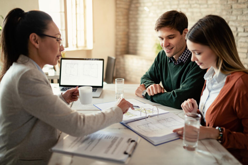 smiling couple insurance agent going through real estate plans during meeting office focus is man - Home Equity Calculator - How Much Can I Borrow Using My Equity?