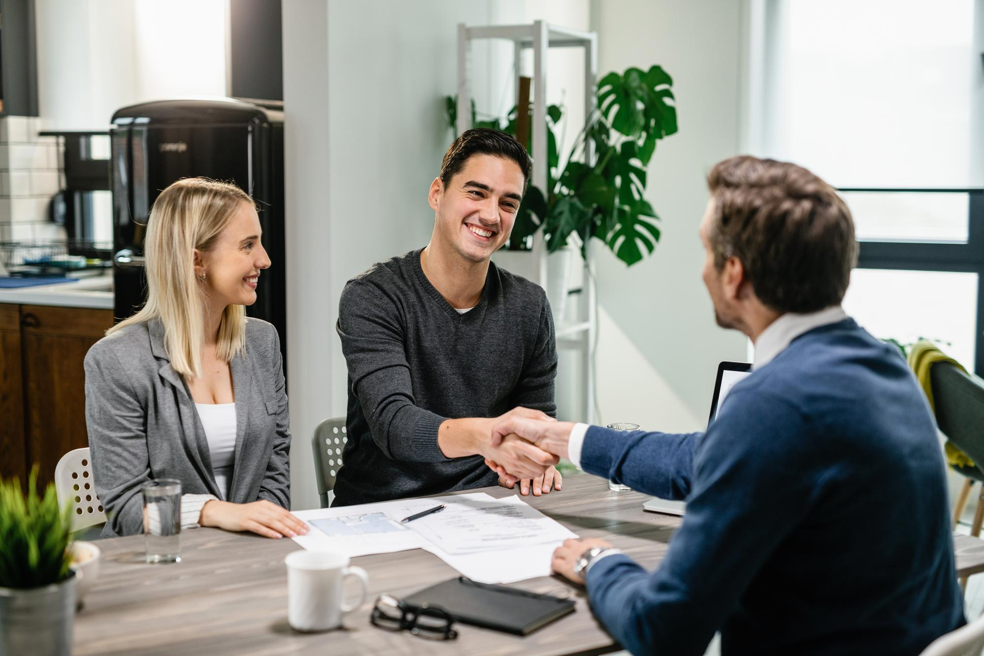 young happy couple making agreement with their financial advisor home men are shaking hands - How Soon After A Consumer Proposal or Bankruptcy Can I Get A Mortgage?