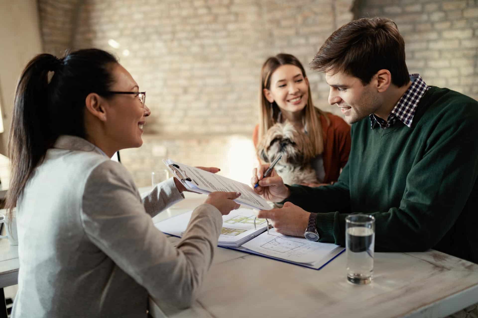 young happy couple signing document while having meeting with real estate agent office focus is man - Mortgage Arrears - What if I Miss A Mortgage Payment?